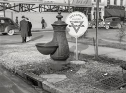 December 1940. Columbus, Georgia. "Water trough and Y.M.C.A. welcome sign in square in center of town." A cast-iron horse-watering fountain with an attachment for dogs, squirrels, etc. Medium format acetate negative by Marion Post Wolcott. View full size.