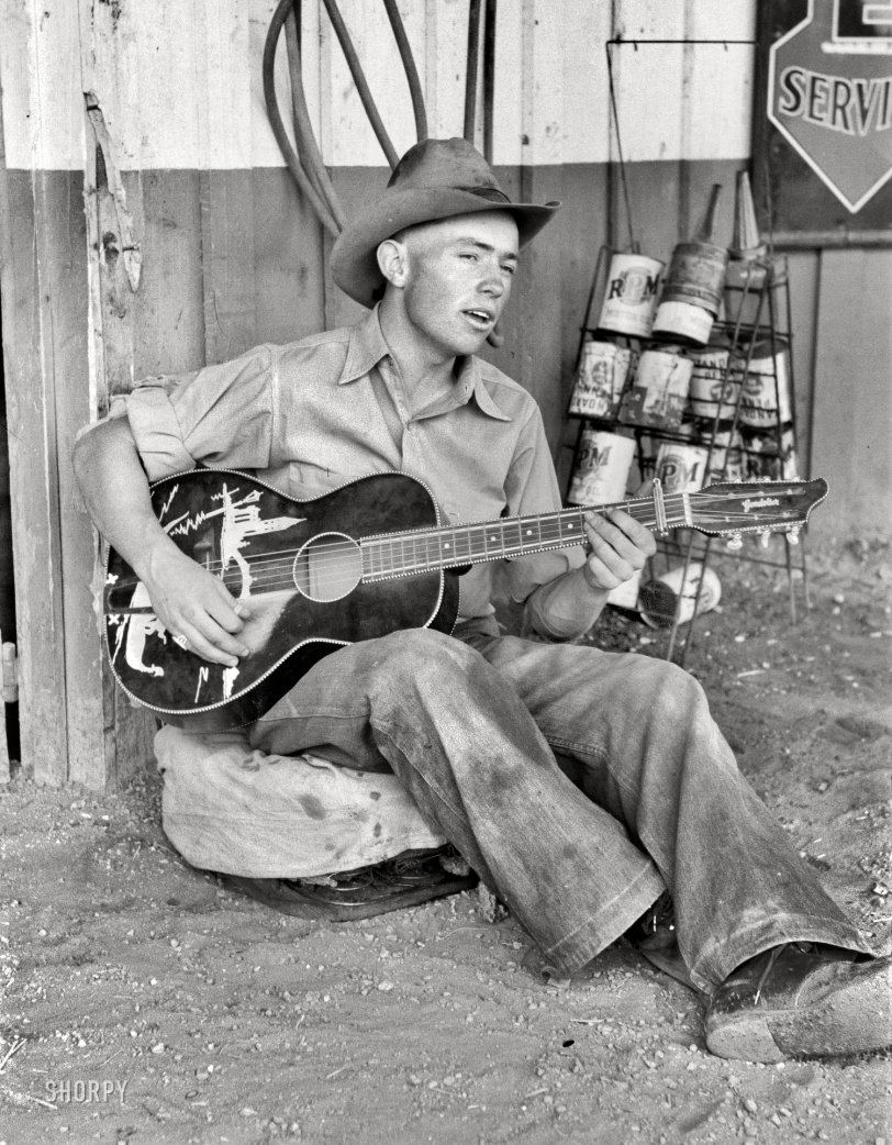 June 1940. Pie Town, New Mexico. "Farm boy playing guitar in front of the filling station and garage." 35mm nitrate negative by Russell Lee. View full size.